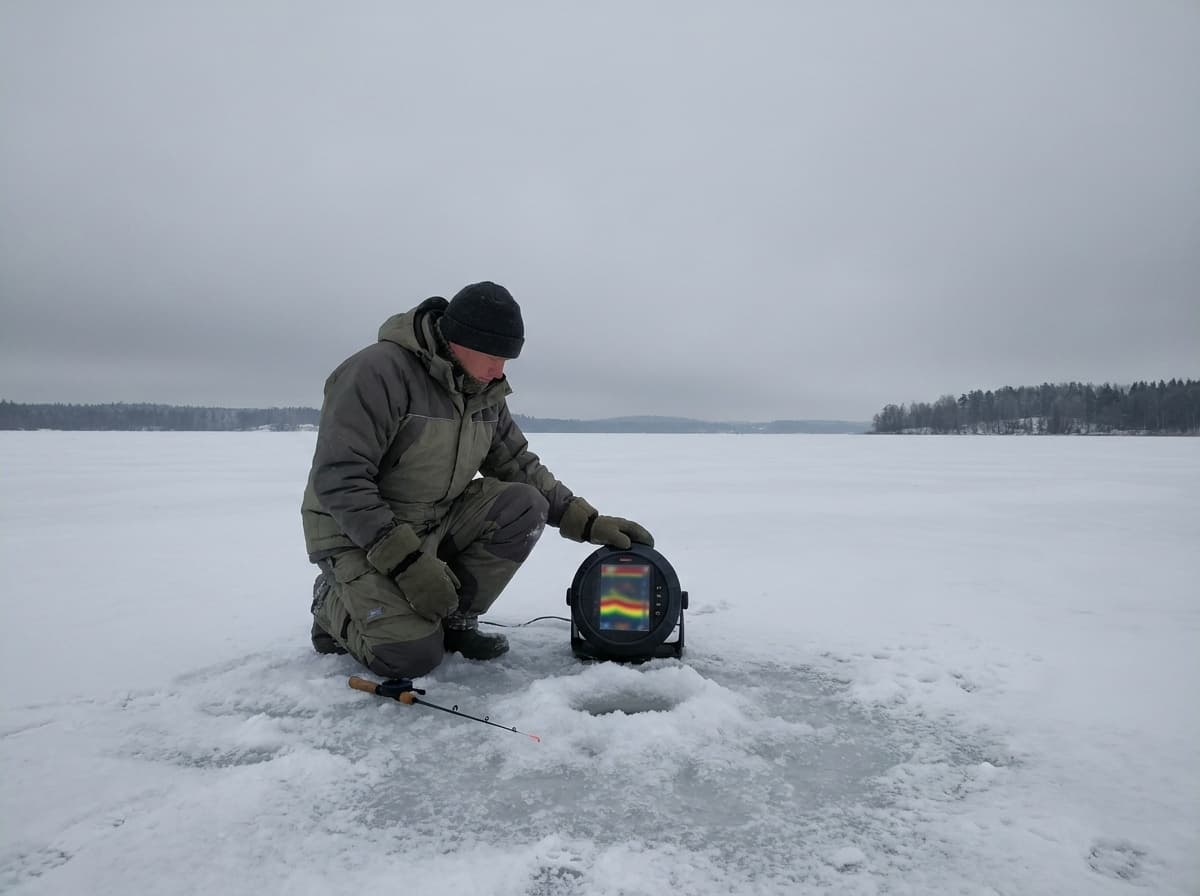 Gloved angler studying an unbranded flasher display beside an ice hole