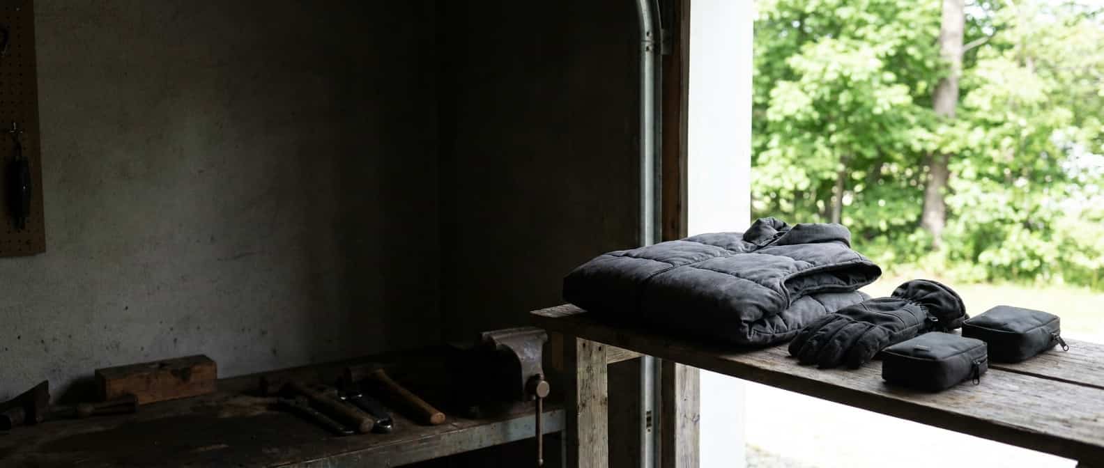 Heated vest, gloves, and battery pouches are stored on a workshop shelf in summer daylight
