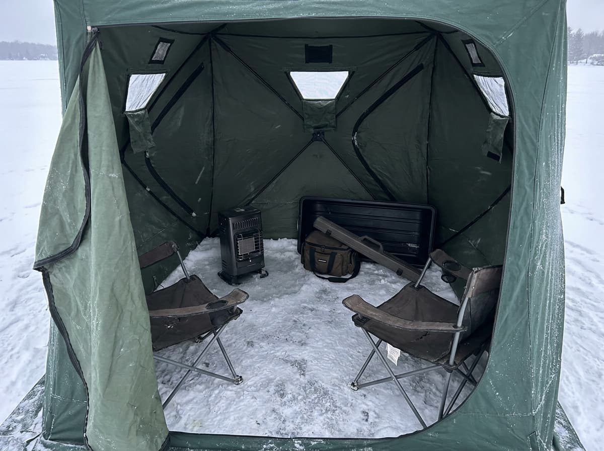 Organized ice-shelter interior with heater, seating, sled, and open working space